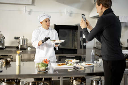 Man records on phone the process of cooking by asian chef in a professional kitchenの写真素材
