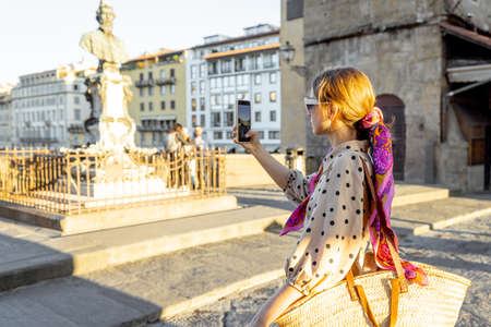 Woman takes photo on phone while visiting famous old bridge, called Ponte Vecchio, in Florence. Concept of traveling italian landmarks. Stylish woman with colorful shawl and sunglassesの写真素材