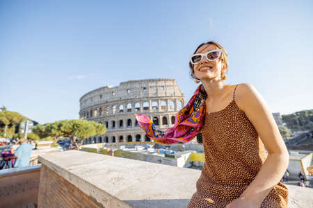 Portrait of a cheerful woman on background of Coliseum in Rome on a summer time. Concept of visiting famous landmarks and travel Italy. Girl wearing dress and colorful shawlの写真素材