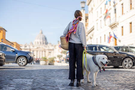 Stylish woman walks with a dog on the street on background of saint Peters cathedral in Rome. Concept of italian lifestyle and travelの写真素材