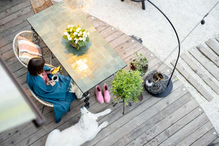 Woman in plaid sitting by the table, relaxing on home terrace with her dog. View from aboveの写真素材