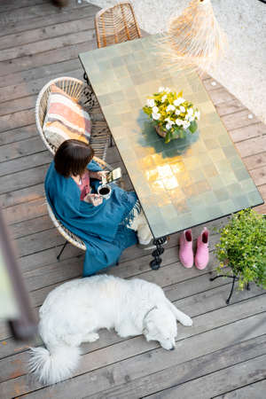 Woman in plaid sitting by the table, relaxing on home terrace with her dog. View from aboveの写真素材