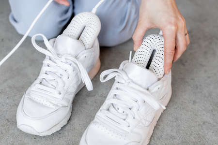 Woman inserting electric dryer into her white sneakers, close-up on shoes. Concept of household technologies and smart gadgetsの写真素材