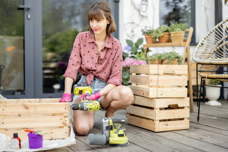 Young cheerful housewife makes wooden boxes, twisting them with a screwdriver while sitting on...
