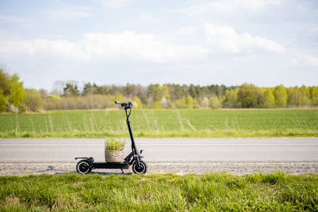 Electric scooter with flowerpot stands on a field road during sunny day. Concept of sustainability and eco-friendly transportationの写真素材