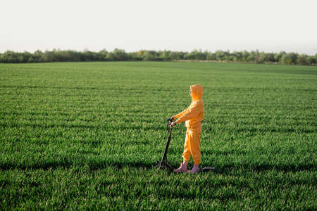 Young person in overalls riding electric scooter on green field during sunset. Concept of sustainability and eco-friendly lifestyleの写真素材