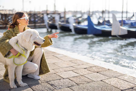 Young woman walking with dog on famous saint Marks square in Venice. Concept of visiting italian landmarks and travel. Woman wearing coat and shawl in italian styleの写真素材