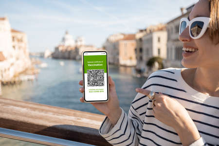 Young woman showing smart phone with qr code of vaccination certificate while traveling in Venice. Concept of social requirements and rules during a pandemic for travelersの写真素材