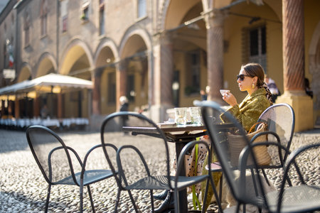 Stylish woman sitting at outdoor cafe in the old town of Bologna city. Italian measured lifestyle...