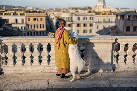 Woman enjoys beautiful cityscape of old Rome city, standing back with her dog on the top of Spanish steps in the morning. Concept of italian lifestyle and travelの写真素材