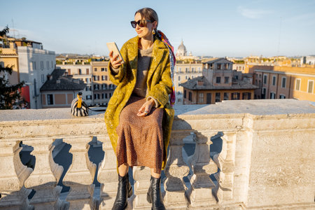 Woman enjoying beautiful morning cityscape of Rome, taking photo on phone, while sitting on the top of famous Spanish steps. Concept of italian lifestyle and travelの写真素材