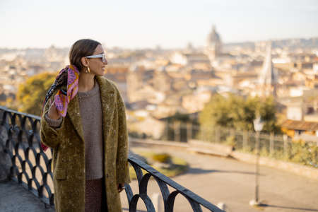 Woman enjoying beautiful morning cityscape of Rome, walking in Villa Borghese Park. Old fashioned woman wearing coat with colorful shawl in hair. Concept of italian lifestyle and travelの写真素材