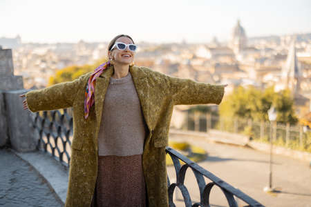 Woman enjoying beautiful morning cityscape of Rome, walking in Villa Borghese Park. Old fashioned woman wearing coat with colorful shawl in hair. Concept of italian lifestyle and travelの写真素材