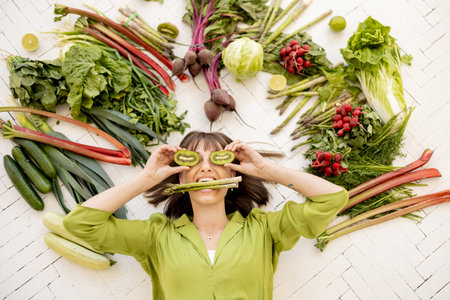 Portrait of a young cheerful woman with lots of fresh vegetables, fruits and greens above her head, top view. Concept of vegan food and healthy lifestyleの写真素材