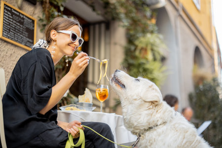 Woman eating pasta with her cute white dog at the restaurant outdoors. Concept of friendship with...