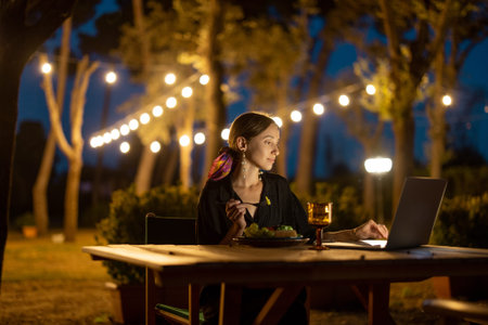 Caucasian woman watching something on laptop computer at evening time outdoors. Young woman sitting...