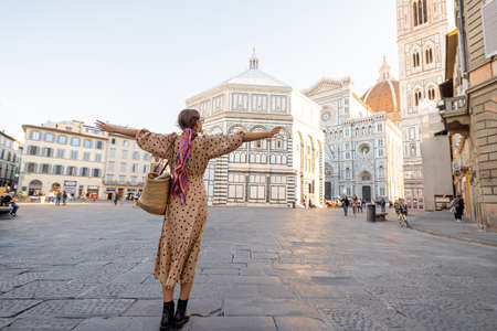 Woman enjoys beautiful view on famous Duomo cathedral in Florence, standing on empty cathedral square during morning time. Stylish woman visiting italian landmarks. Traveling Italy conceptの写真素材