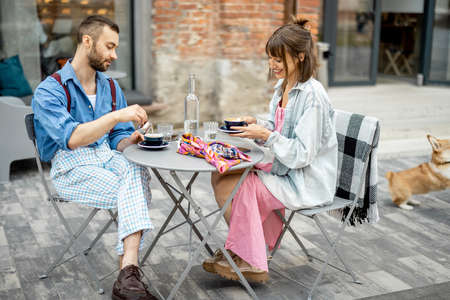 Stylish man and woman have delicious breakfast, eating and talking at cafe terrace. Friends spending time together during a breakfastの写真素材