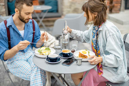 Stylish man and woman have delicious breakfast, eating and talking at cafe terrace. Friends spending time together during a breakfastの写真素材
