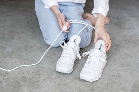 Woman inserting electric dryer into her white sneakers, close-up on shoes. Concept of household technologies and smart gadgetsの写真素材