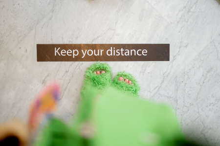 Woman in fluffy slippers standing near the inscription KEEP YOUR DISTANCE on the floor at some pulic area. Concept of social distancingの写真素材