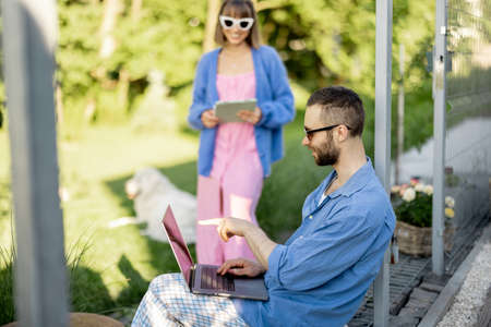 Young stylish couple work or spend leisure time with laptop computer on porch of country house on nature. Concept of remote work on natureの写真素材