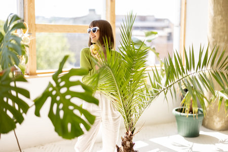 Portrait of a young woman stands between green plants in the room