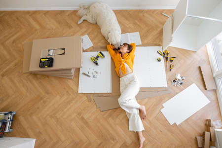 Young woman lies on floor with her cute dog, resting while making repairing at new apartment, top view. Young woman assembling furniture by herself. DIY conceptの写真素材