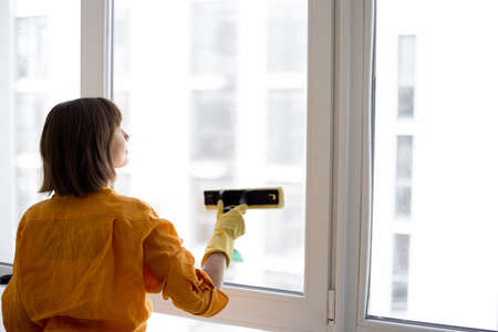 Young housewife or a cleaning company employee washes window with special tool in apartment.の写真素材