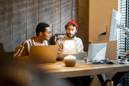 Two men with different nationality working on computers, sitting together at cozy home office....