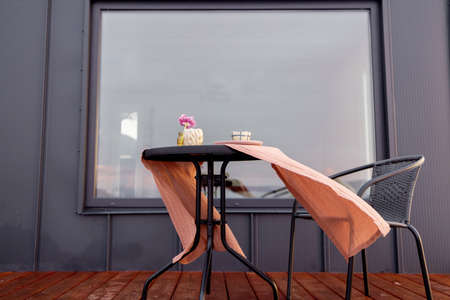Terrace of a tiny house with table covered with tablecloth fluttering in the wind. Concept of small modern cabins for rest and escape to natureの写真素材