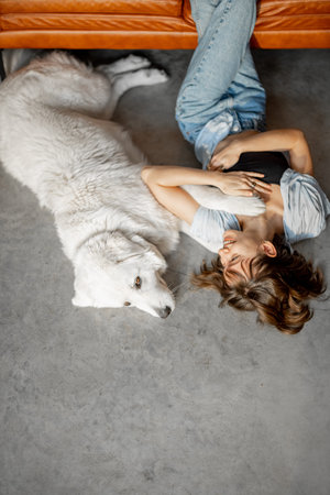 Woman lying relaxed with her adorable dog on the floor near couch at home. Concept of home comfort...