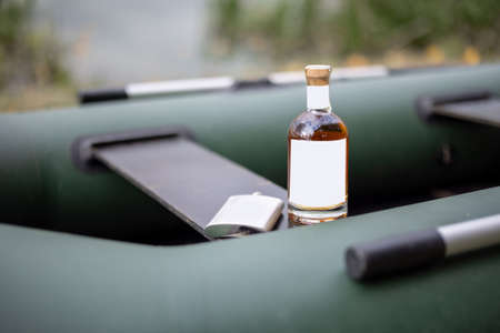 Bottle with strong alcohol and flask on rubber boat outdoors. Bottle with blank label to copy paste. Mockup image for branding drinkの写真素材