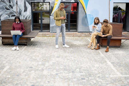 Multiracial students with digital gadgets outdoors. Concept of students lifestyle. Idea of remote and e-learning. Young guys and girls at university campusの写真素材