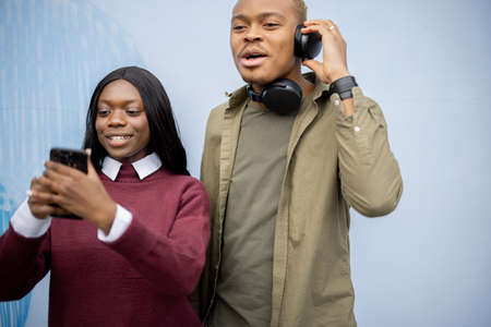 Young black couple taking selfie on smartphone. Smiling girl and serious man. Concept of spending time together. People on blue backgroundの写真素材