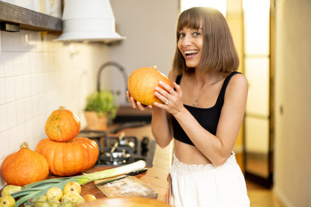 Portrait of a cheerful woman holds pumpkin vegetables while cooking healthy food in kitchen. Concept of vegetarian food and autumn pumpkin menuの写真素材