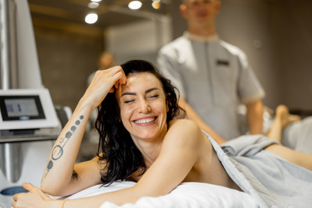 Portrait of happy adult woman lying on medical couch during vacuum roller massage procedure at medical beauty centreの写真素材