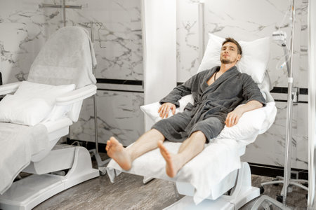 Man in a bathrobe is waiting for a blood washing and vitaminization procedure or taking blood for tests in a medical center. Lying relaxed on comfortable medical couchの写真素材