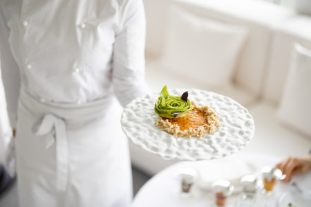 Chef holds a plate with delicious vegetarian meal decorated with flower made of avocado at restaurant of haught cuisine, close-up on dishの写真素材