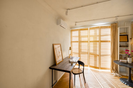 Cozy worplace with wooden table, chair and window blinds on background in bright living room at home. Wide view with copy space on the wallの写真素材