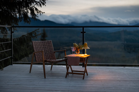 Spacious terrace with cozy table, chair and lamp highly in mountains at dusk. Cozy lounge place for...
