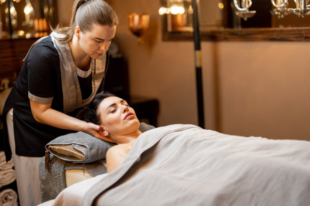 Woman happy to receive relaxation soulder massage from professional masseuse indoors. Beautiful adult brunette woman at spa salonの写真素材