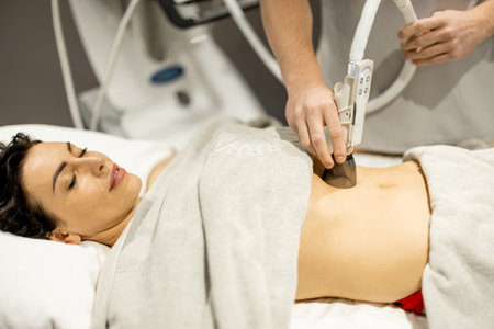 Woman receiving vacuum roller massage for her belly at medical beauty centre. Anti-cellulite and lymphatic drainage massage procedureの写真素材