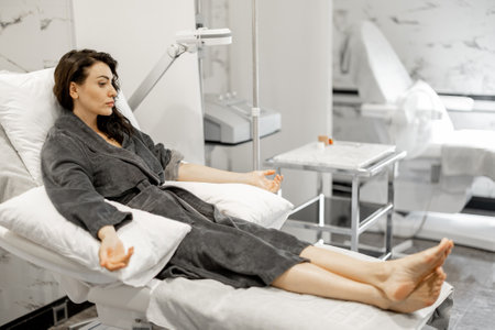 Woman in a bathrobe is waiting for a blood washing and vitaminization procedure or taking blood for tests in a medical center. Lying relaxed on comfortable medical couchの写真素材