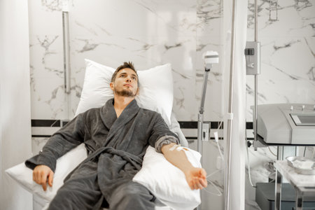 Man in bathrobe lying on medical couch during blood wash procedure with catheter in his arm at medical centreの写真素材