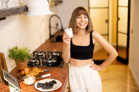Portrait of young and cheerful woman whiich drinks dairy beverage during a breakfast time on kitchen of modern apartment. Wellness and domestic lifestyle conceptの写真素材