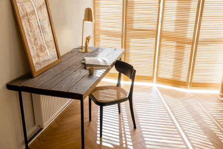 Cozy worplace with wooden table, chair and window blinds on background in bright living room at homeの写真素材