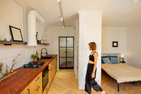 Interior of stylish studio apartment with kitchen and bedroom in white and beige tones in loft style and woman in motionの写真素材