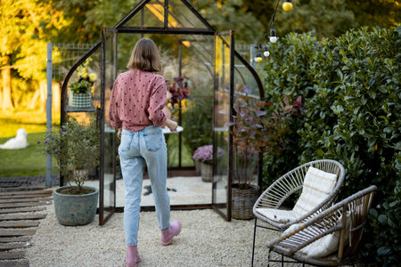 Woman walks into glasshouse for growing plants and flowers, gardening at backyardの写真素材