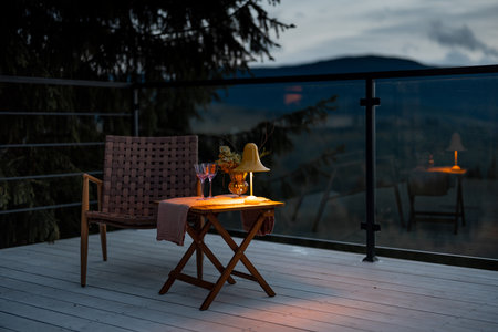 Spacious terrace with cozy table, chair and lamp highly in mountains at dusk. Cozy lounge place for rest at house on natureの写真素材